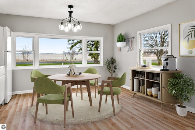 dining area featuring a textured ceiling, plenty of natural light, a notable chandelier, and light hardwood / wood-style flooring