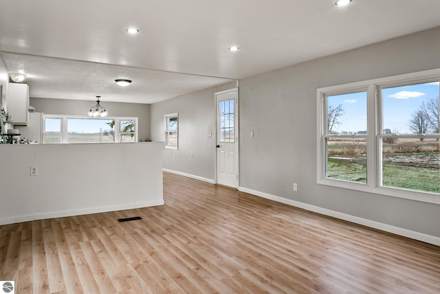 unfurnished living room featuring an inviting chandelier and light hardwood / wood-style flooring