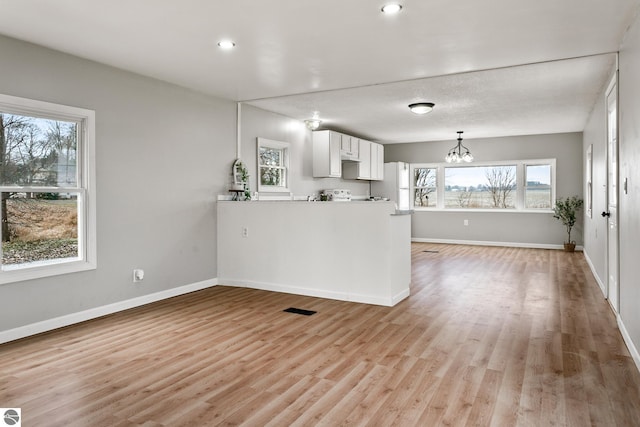 kitchen with a wealth of natural light, white cabinetry, a notable chandelier, and light wood-type flooring