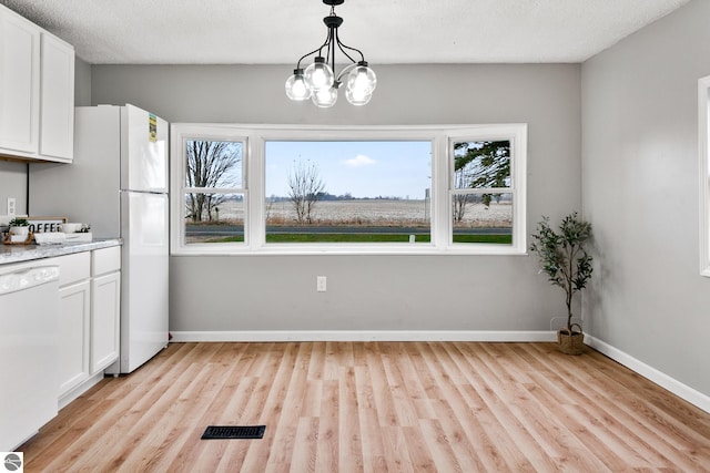 unfurnished dining area featuring light hardwood / wood-style flooring, a textured ceiling, and a notable chandelier