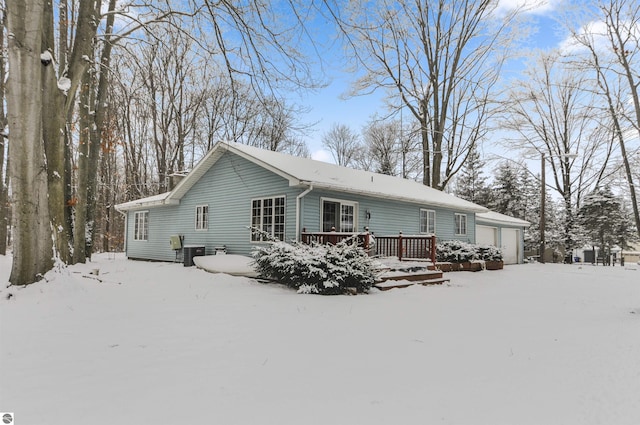 snow covered back of property featuring central air condition unit and a garage