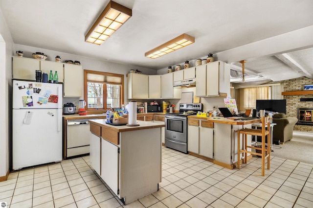 kitchen with a center island, a brick fireplace, beamed ceiling, brick wall, and white appliances