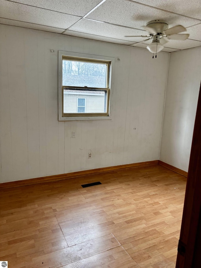 spare room with light wood-type flooring, ceiling fan, a paneled ceiling, and wood walls