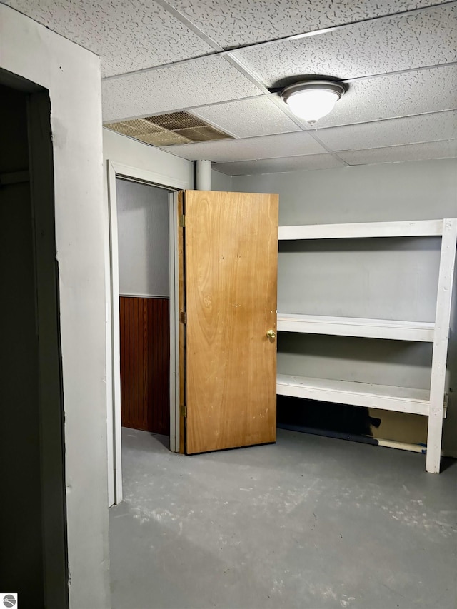 basement with a drop ceiling and wooden walls