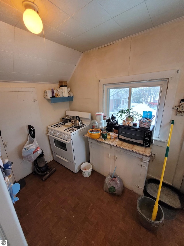 kitchen with dark parquet floors, tile countertops, vaulted ceiling, and white range with gas cooktop