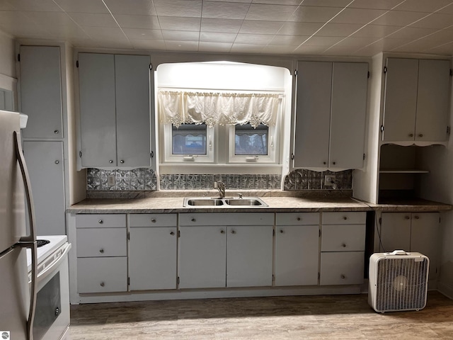 kitchen with white range with electric cooktop, sink, decorative backsplash, light hardwood / wood-style floors, and stainless steel refrigerator