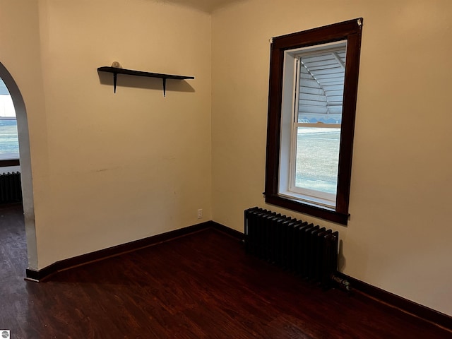 empty room with radiator heating unit and dark wood-type flooring