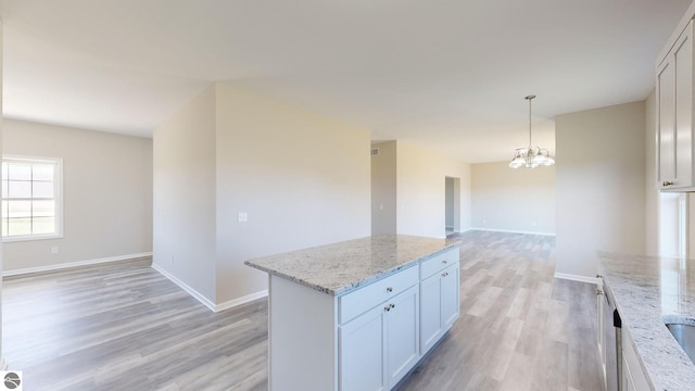 kitchen with an inviting chandelier, decorative light fixtures, a kitchen island, light stone counters, and white cabinetry