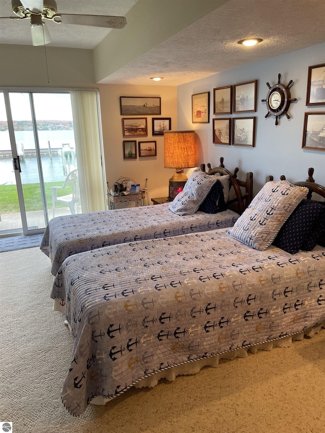 carpeted bedroom featuring access to outside, ceiling fan, a water view, and a textured ceiling