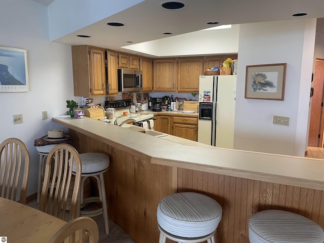 kitchen with a kitchen bar, kitchen peninsula, lofted ceiling, and white appliances