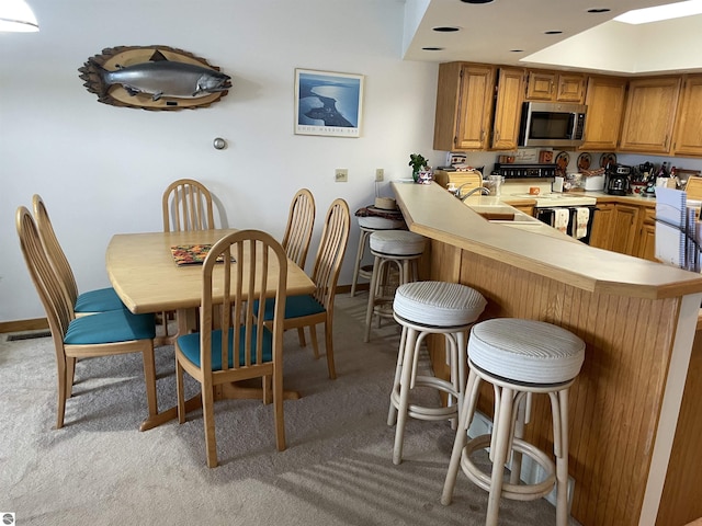 kitchen featuring a kitchen breakfast bar, white electric range, sink, light colored carpet, and kitchen peninsula