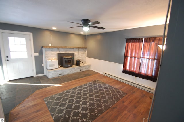 living room with dark hardwood / wood-style floors, ceiling fan, a wood stove, and baseboard heating