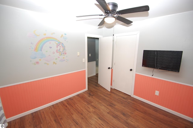 unfurnished bedroom featuring ceiling fan, dark hardwood / wood-style flooring, and wooden walls