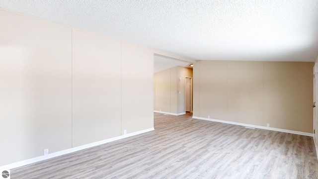 empty room with vaulted ceiling, light hardwood / wood-style floors, and a textured ceiling