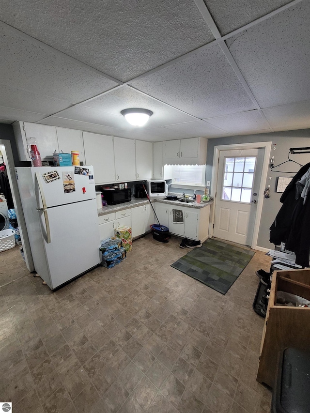 kitchen with a paneled ceiling, white appliances, sink, washer / clothes dryer, and white cabinetry