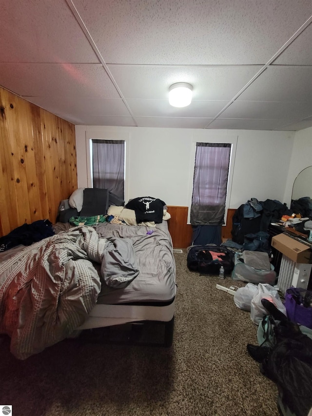 bedroom with wooden walls, a drop ceiling, and carpet