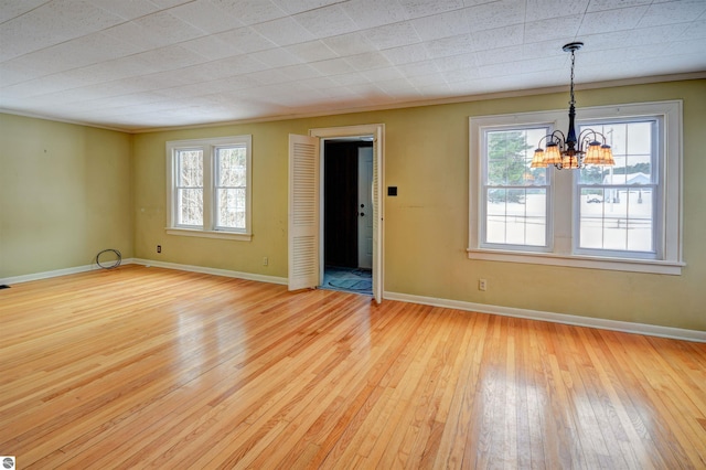 empty room with plenty of natural light, an inviting chandelier, and light hardwood / wood-style floors