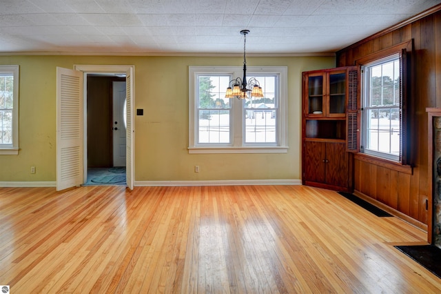 unfurnished dining area with wooden walls, a chandelier, and light wood-type flooring