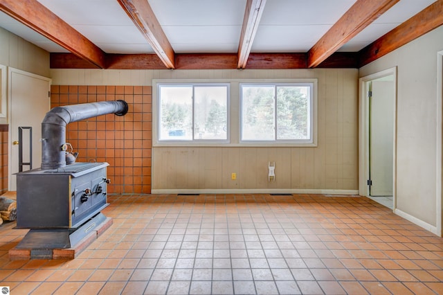 tiled living room featuring a wood stove, beam ceiling, and a healthy amount of sunlight