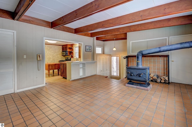 unfurnished living room featuring a wood stove, wood walls, beamed ceiling, and light tile patterned flooring