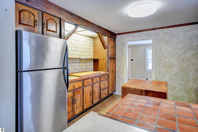 kitchen featuring light tile patterned floors, tile countertops, crown molding, and stainless steel refrigerator