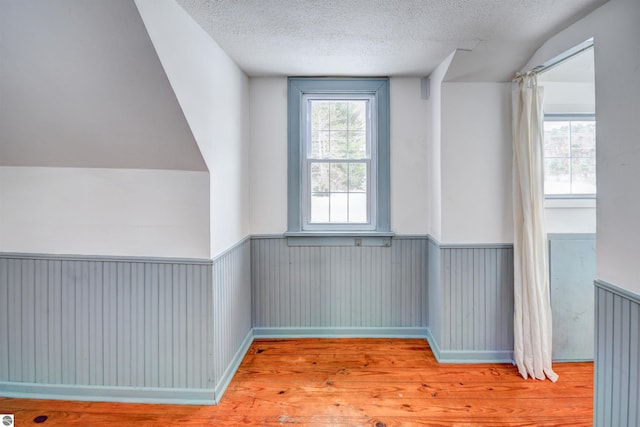 additional living space with light wood-type flooring, a textured ceiling, and lofted ceiling