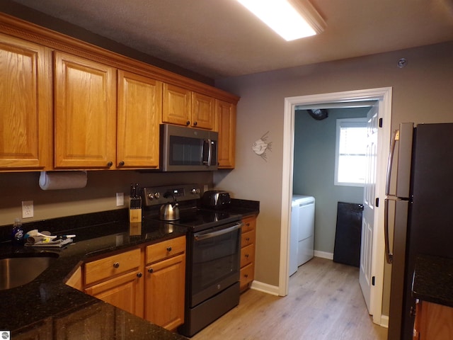 kitchen featuring appliances with stainless steel finishes, dark stone counters, sink, washer / dryer, and light hardwood / wood-style floors