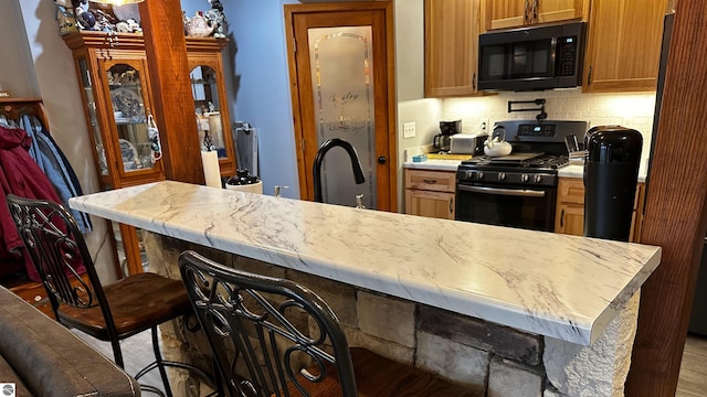 kitchen with a breakfast bar, backsplash, sink, and black appliances