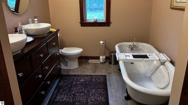 bathroom featuring a washtub, wood-type flooring, vanity, and toilet