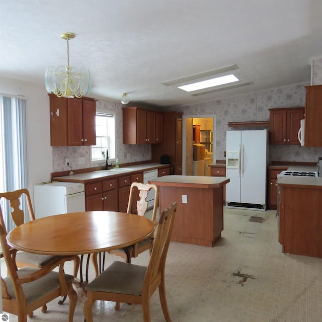 kitchen featuring white appliances, sink, pendant lighting, a notable chandelier, and a center island