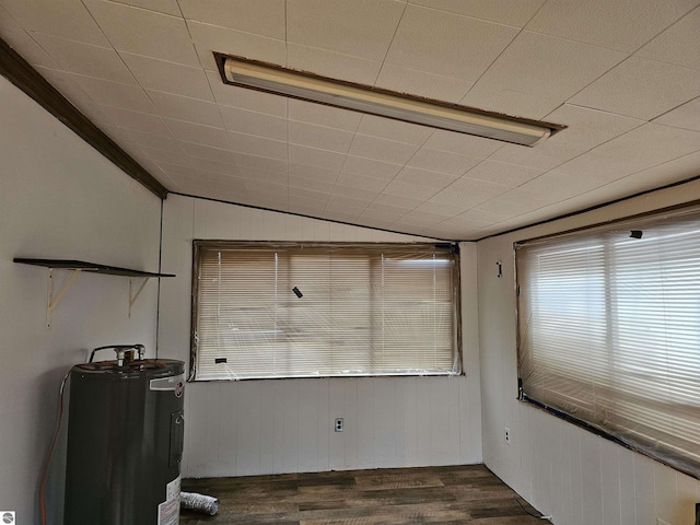 empty room featuring lofted ceiling, dark hardwood / wood-style flooring, electric water heater, and wooden walls