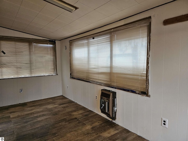 unfurnished room with dark wood-type flooring, wooden walls, and heating unit