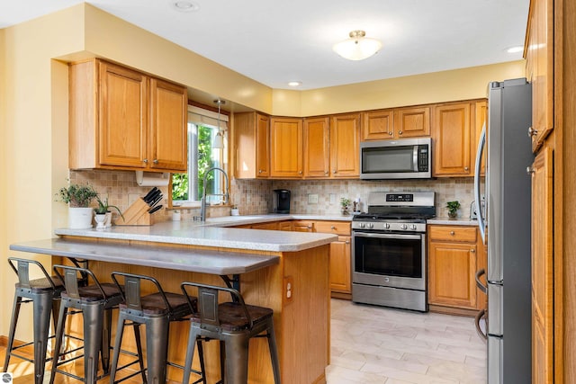 kitchen with kitchen peninsula, appliances with stainless steel finishes, a kitchen breakfast bar, and sink