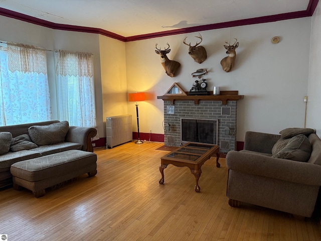 living room with light hardwood / wood-style floors, crown molding, radiator, and a brick fireplace