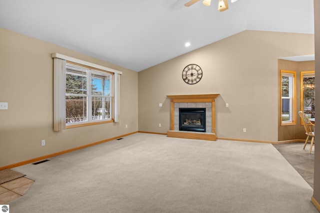 unfurnished living room with ceiling fan, a tiled fireplace, light carpet, and vaulted ceiling