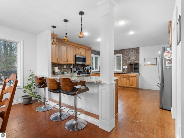 kitchen featuring decorative columns, kitchen peninsula, light stone countertops, and appliances with stainless steel finishes