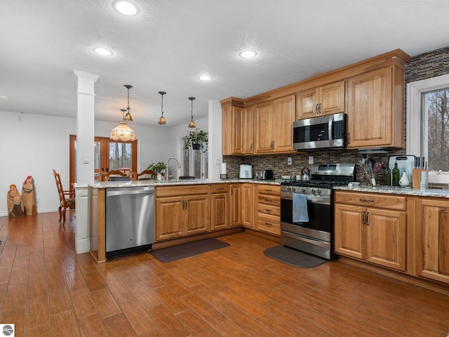 kitchen featuring kitchen peninsula, appliances with stainless steel finishes, light stone counters, and pendant lighting