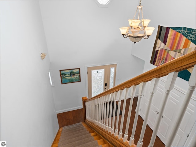 stairs with wood-type flooring and an inviting chandelier