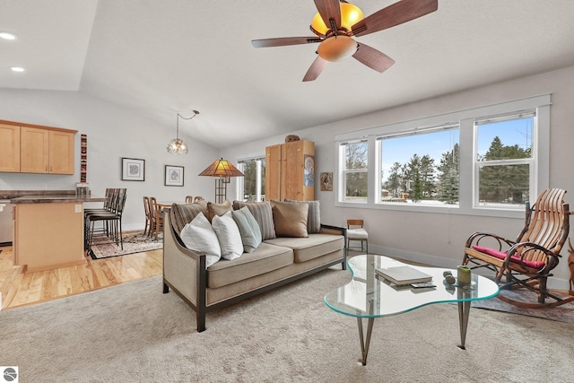 living room featuring ceiling fan with notable chandelier, light wood-type flooring, and vaulted ceiling