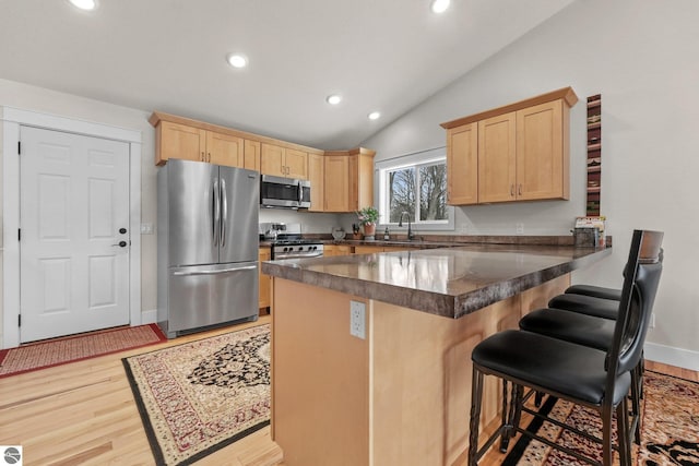 kitchen featuring light brown cabinets, light hardwood / wood-style flooring, a kitchen bar, kitchen peninsula, and stainless steel appliances