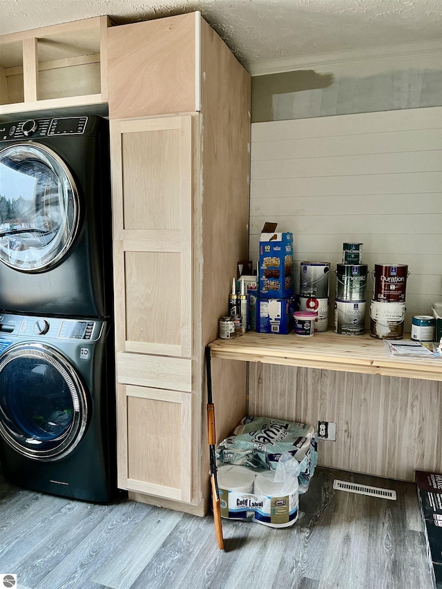 laundry area featuring hardwood / wood-style flooring, stacked washing maching and dryer, and a textured ceiling