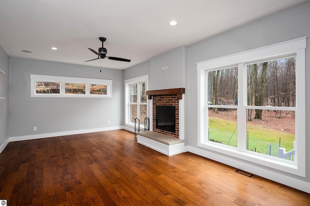 unfurnished living room with ceiling fan, wood-type flooring, and a brick fireplace