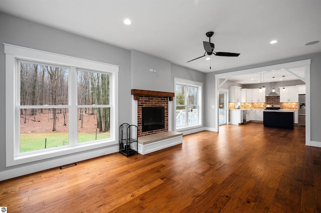 unfurnished living room featuring hardwood / wood-style floors, a brick fireplace, and ceiling fan