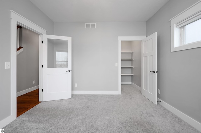 unfurnished bedroom featuring a spacious closet, a closet, and light colored carpet