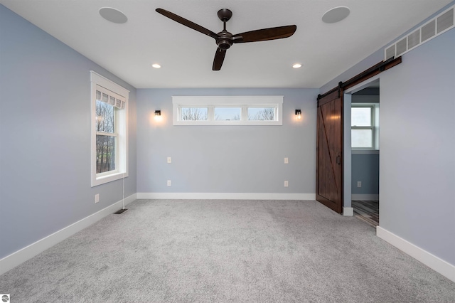 carpeted empty room featuring ceiling fan and a barn door