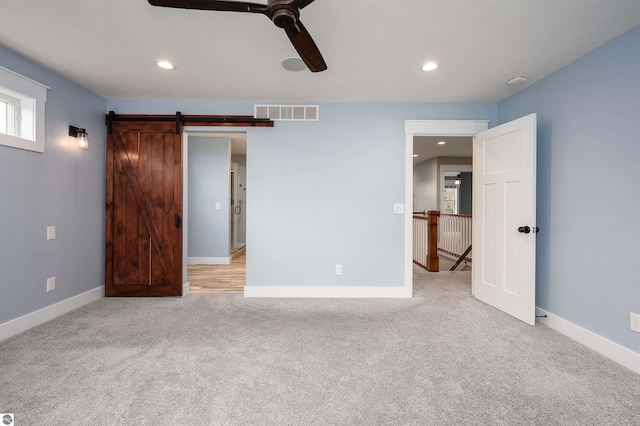 unfurnished bedroom featuring light carpet, a barn door, and ceiling fan