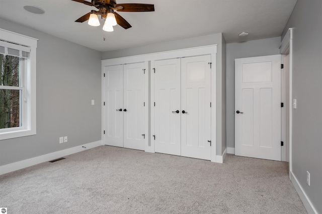 unfurnished bedroom with light carpet, multiple windows, ceiling fan, and multiple closets