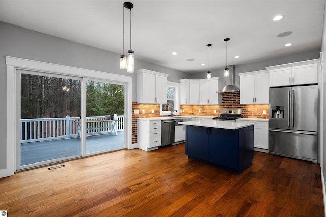 kitchen featuring white cabinetry, wall chimney exhaust hood, hanging light fixtures, and appliances with stainless steel finishes