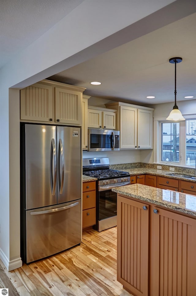 kitchen with sink, light stone counters, light hardwood / wood-style floors, decorative light fixtures, and appliances with stainless steel finishes