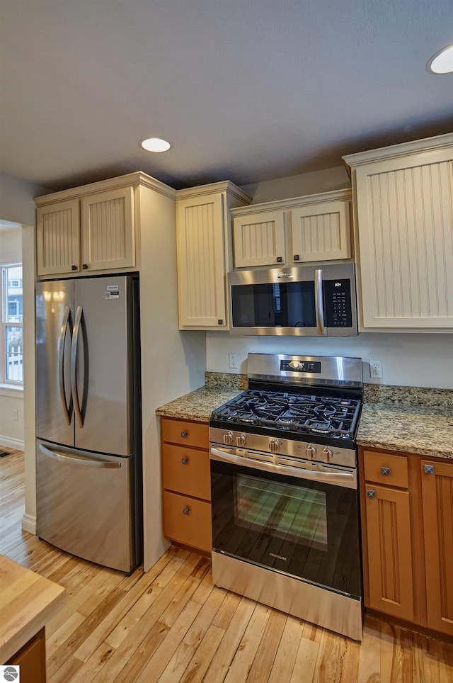 kitchen featuring light stone countertops, appliances with stainless steel finishes, and light hardwood / wood-style flooring